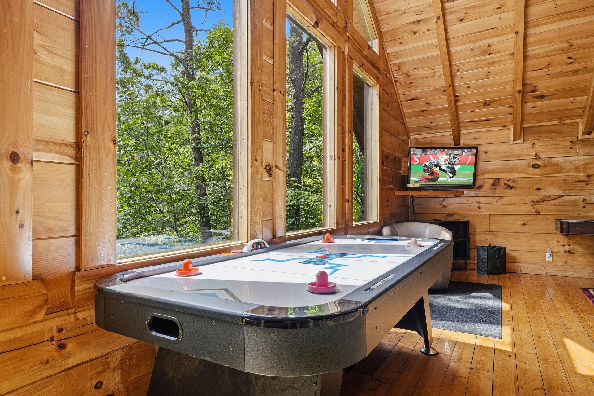 Your game room awaits with air hockey, a mounted TV, and floortoceiling windows framing lush forest views—perfect for friendly competition and relaxation.
