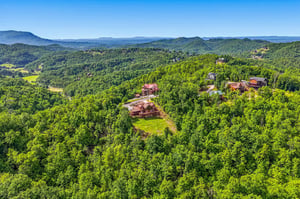 Aerial view of mountain cabins nestled in forested hills with expansive Appalachian ridges stretching to the horizon under clear blue skies.