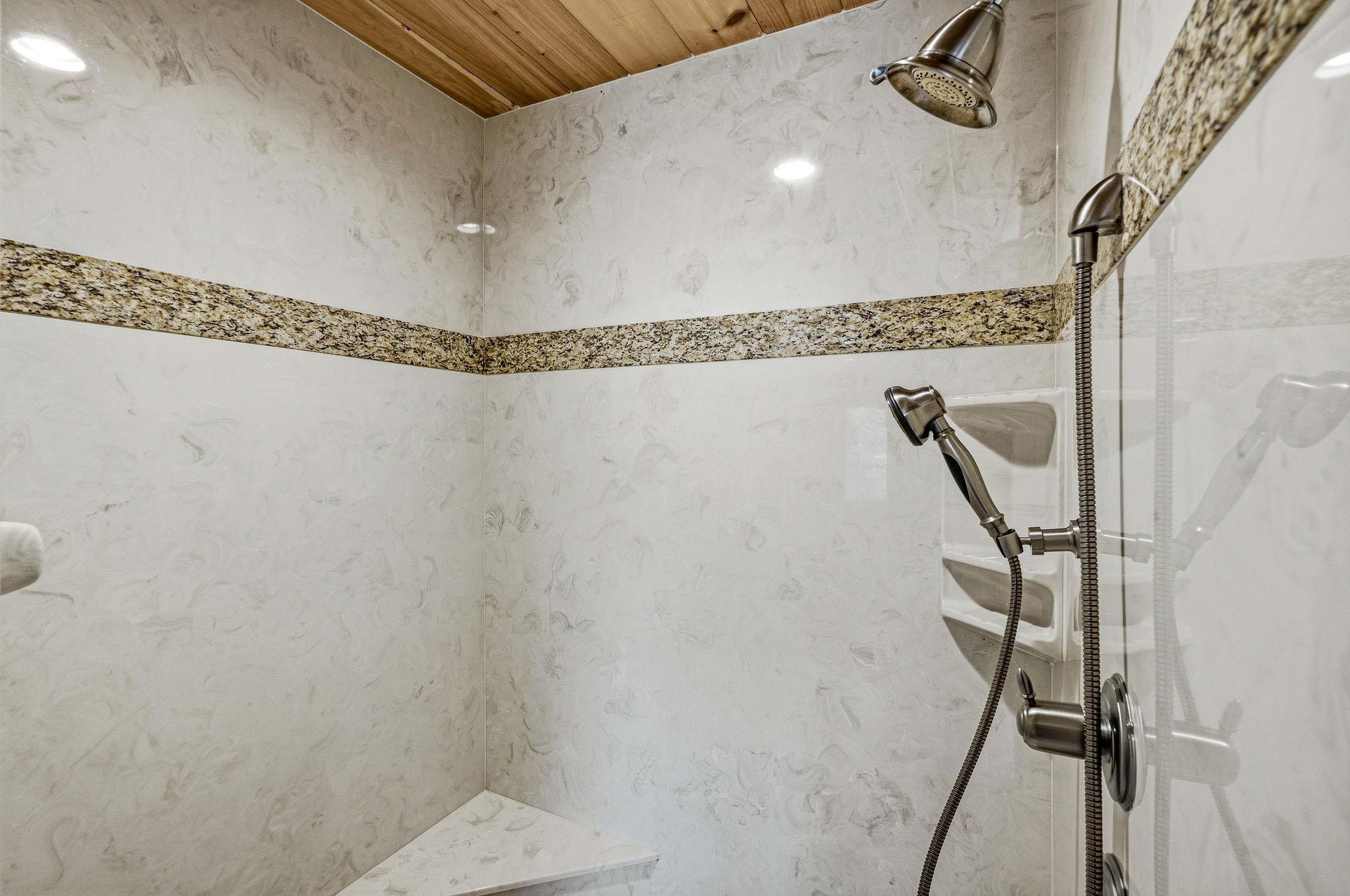Step into your luxurious marble shower with dual rainfall and handheld heads, featuring elegant stone accents and warm wood ceiling details.