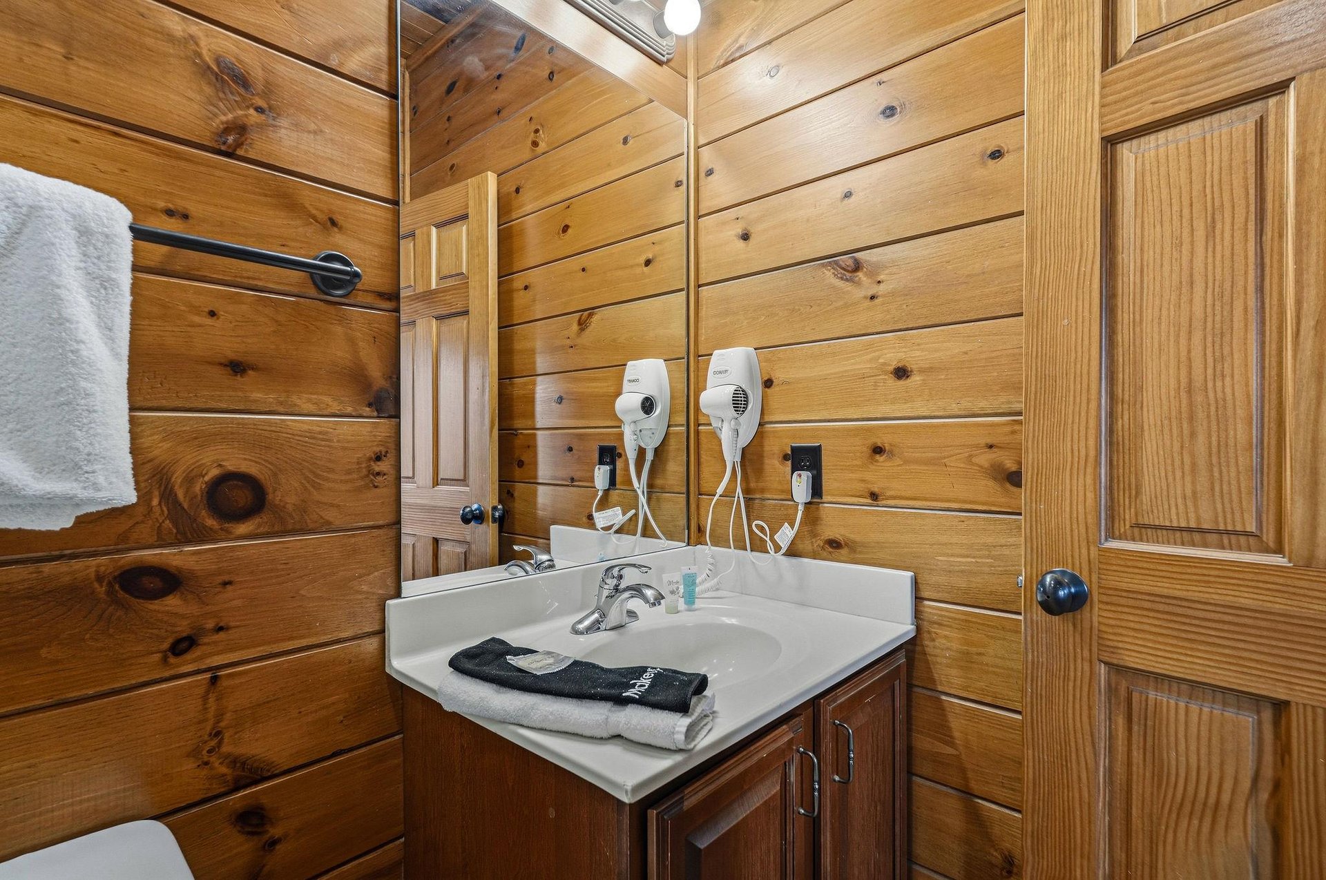 Warm woodpaneled bathroom with a skylight, vanity sink, fresh towels, and hair dryers for your convenience.