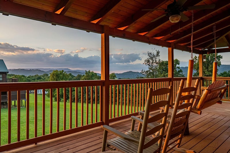 Gentle evening light washes over your private covered deck, where wooden rockers invite quiet moments gazing at layered mountain ridges and lush greenery stretching to the horizon.