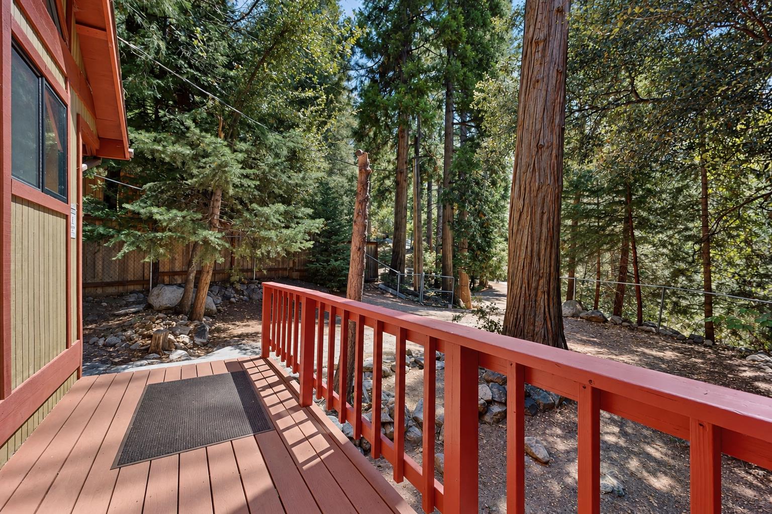 The deck continues around to a shaded entrance, framed by towering redwoods — a peaceful first step into the cabin.
