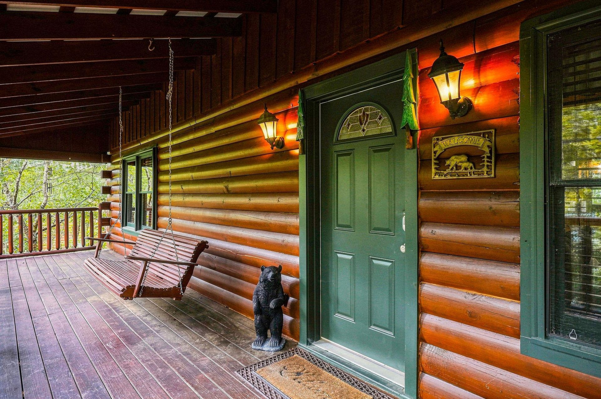 The charming log cabin entrance greets you with rustic elegance—a cozy porch swing invites you to relax while warm lantern light creates an inviting atmosphere for your mountain getaway.