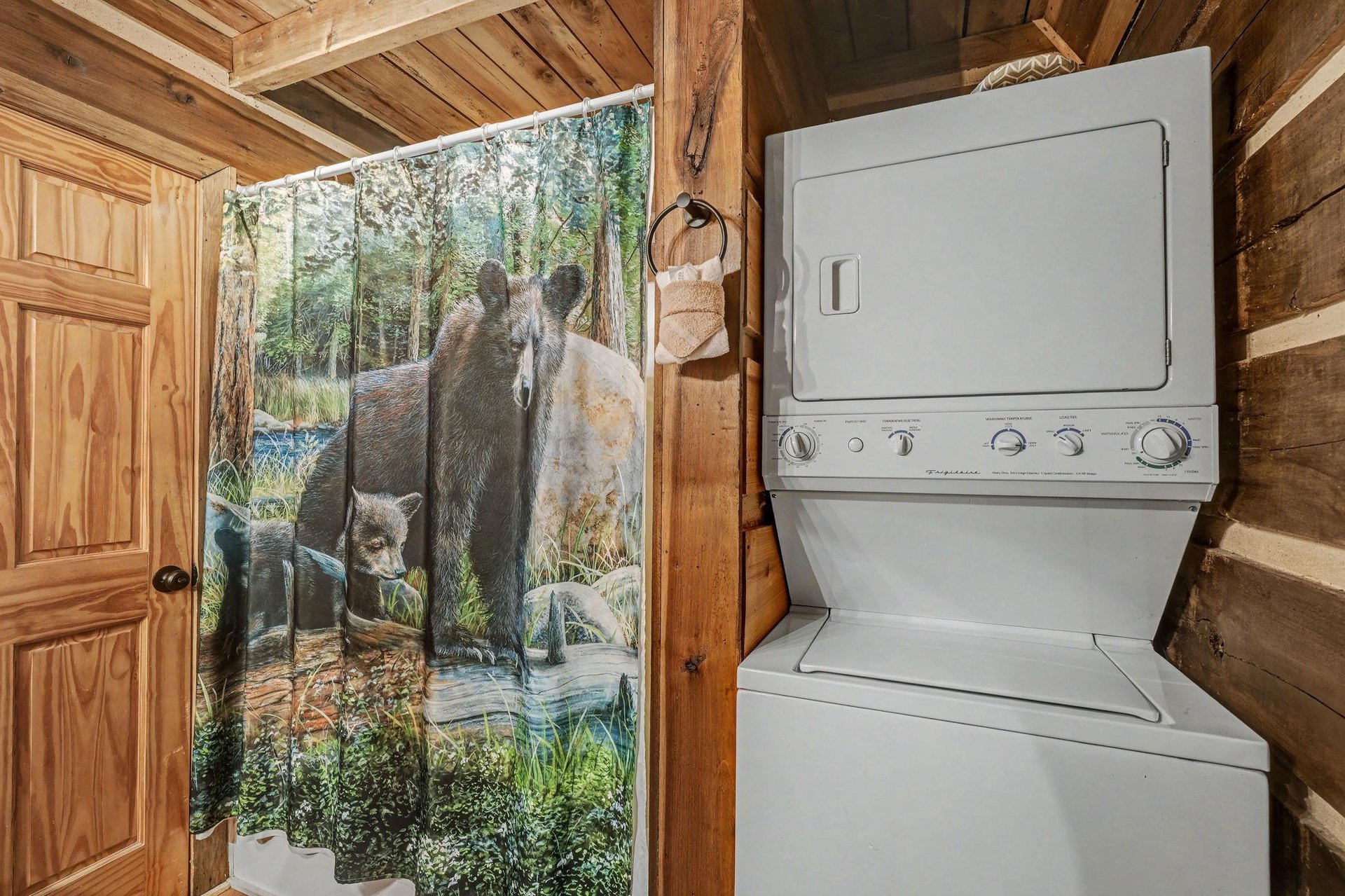 Your private laundry nook features a stacked washerdryer combo beneath rustic wood beams, with charming woodland artwork adding a cozy mountain feel.