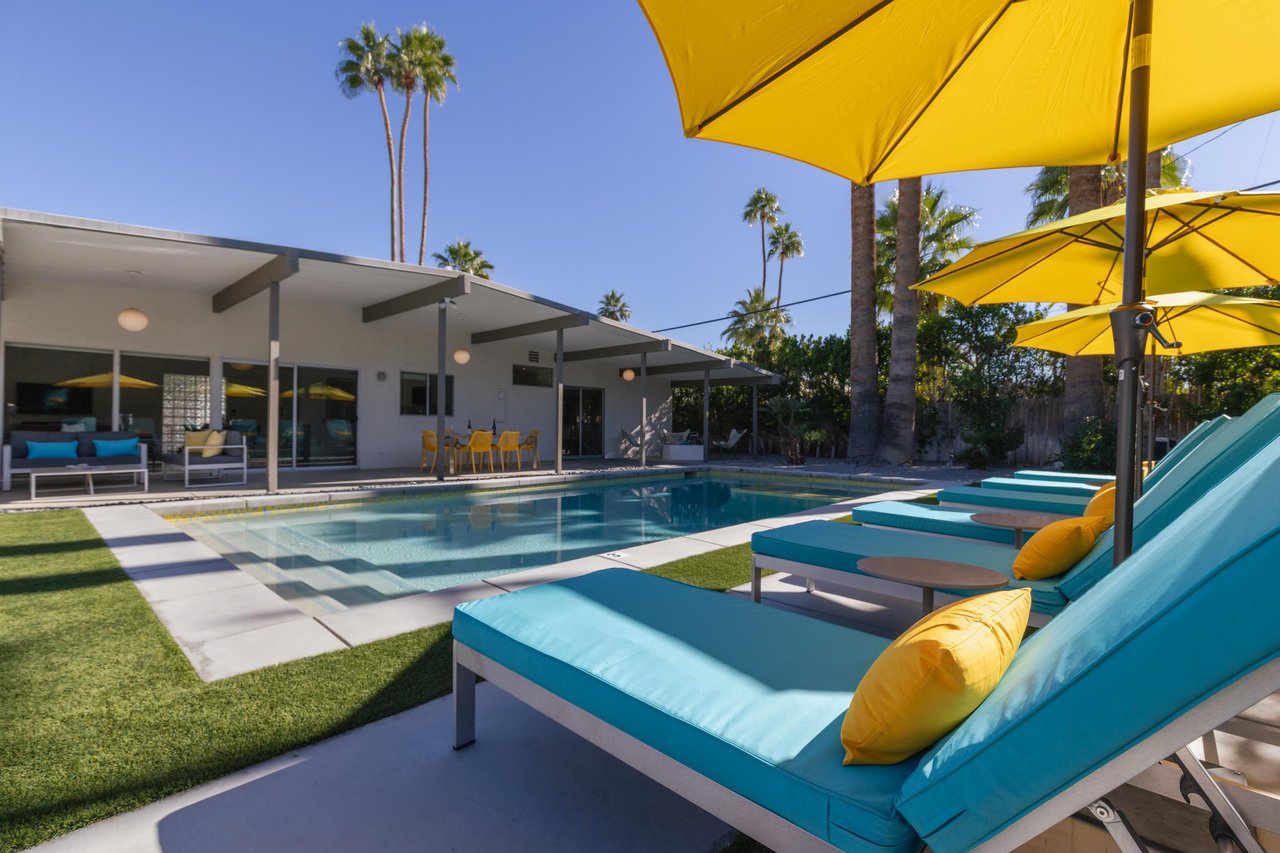 Sink into plush turquoise loungers under sunny yellow umbrellas beside your private pool, with towering palms swaying overhead in this desert oasis.