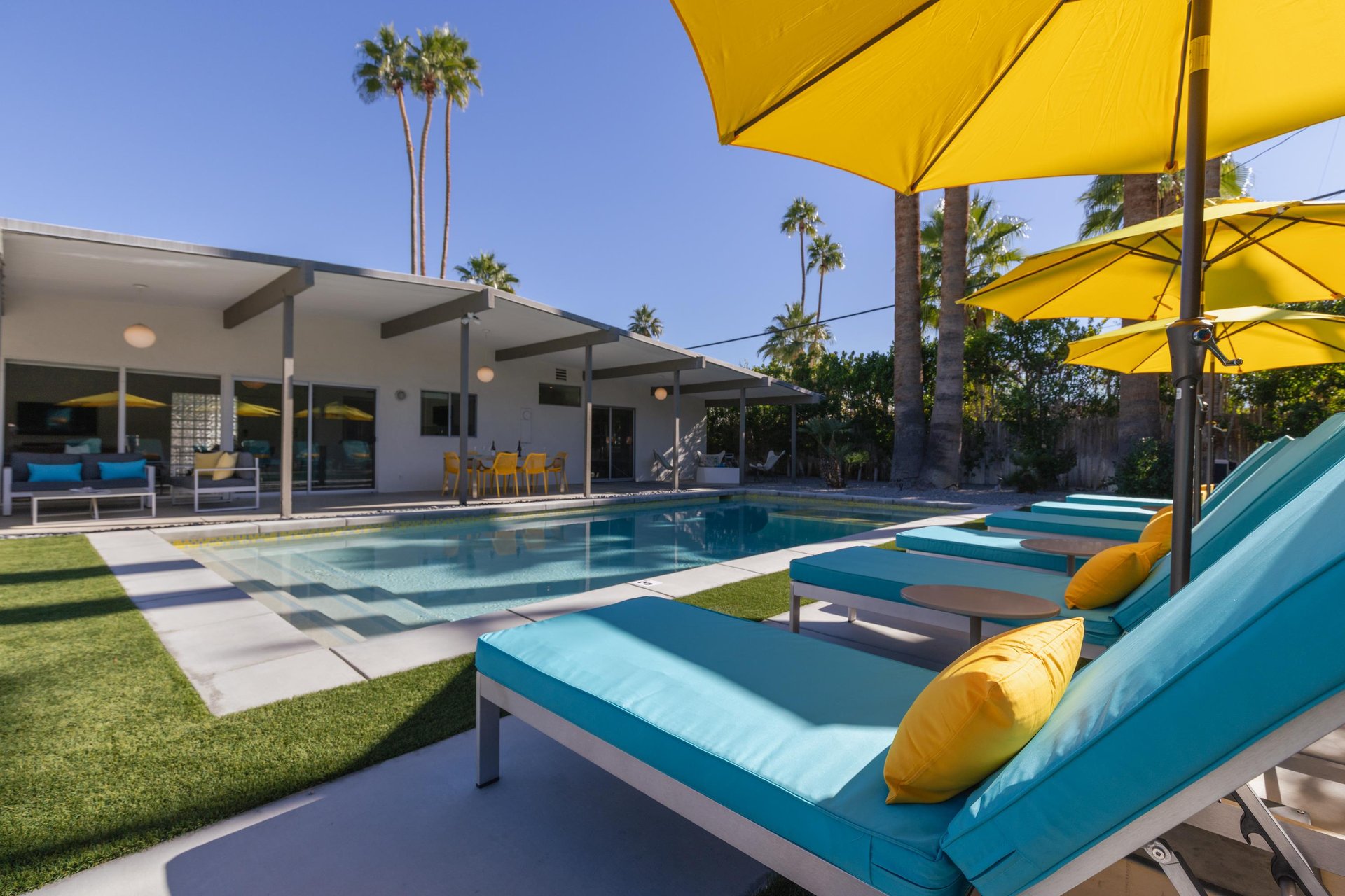 Sink into plush turquoise loungers under sunny yellow umbrellas beside your private pool, with towering palms swaying overhead in this desert oasis.