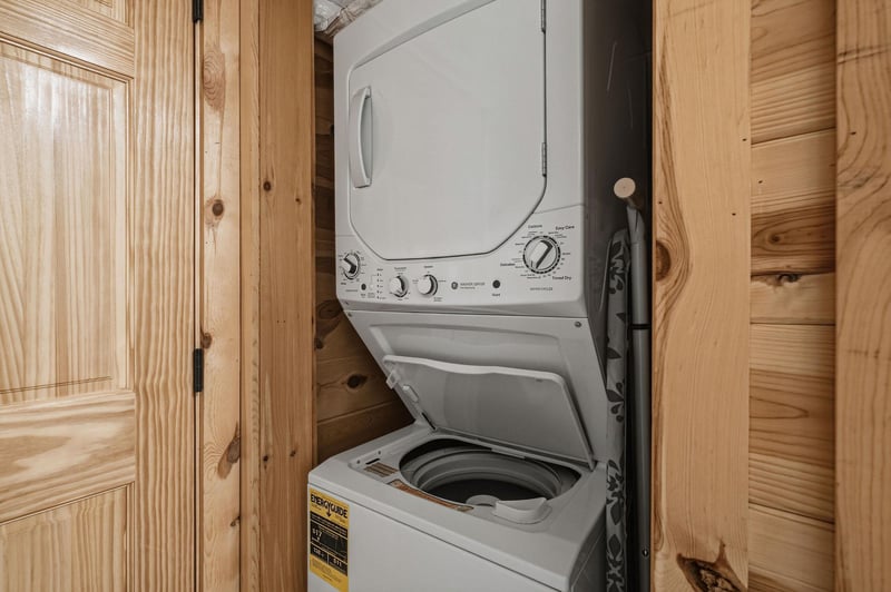 Your laundry needs are covered with this convenient stacked washer and dryer, tucked neatly into its own cozy space surrounded by warm natural wood paneling.