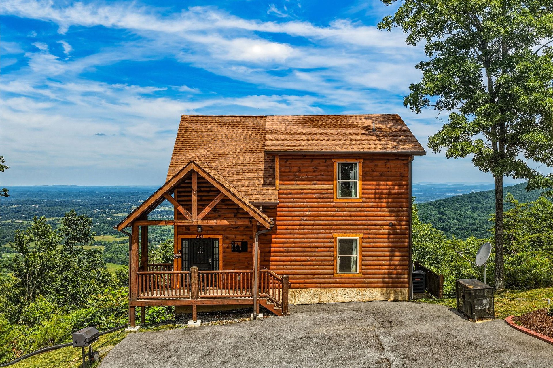 Charming log cabin perched on a mountainside with breathtaking valley views, featuring a welcoming covered porch and surrounded by lush forest greenery.