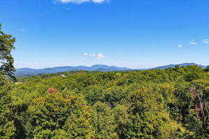 Sweeping mountain vistas stretch across lush forest canopy under clear blue skies, showcasing the propertys scenic surroundings.