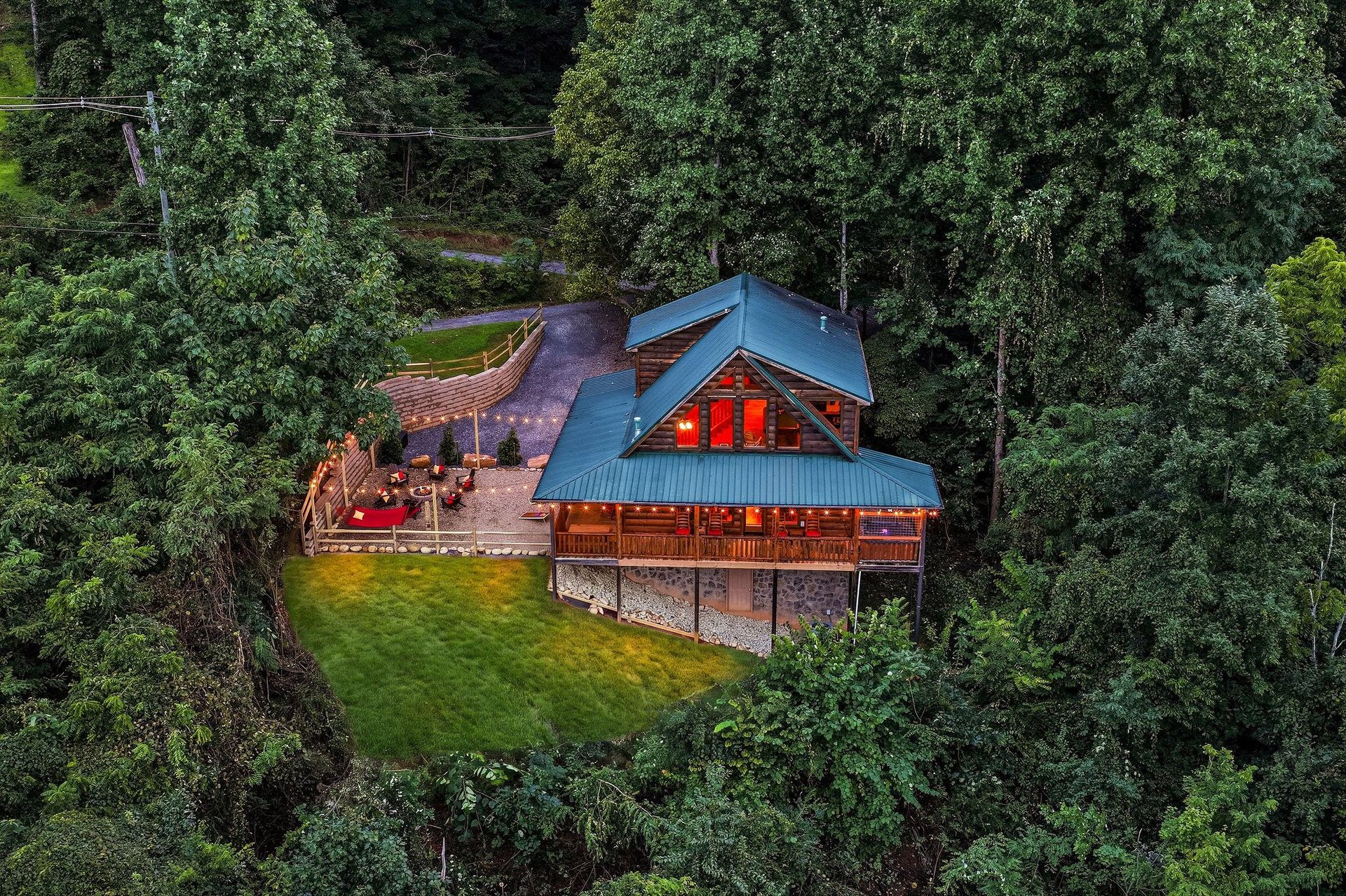 Secluded log cabin retreat nestled in lush wooded surroundings, featuring spacious decks with outdoor seating and glowing evening ambiance.