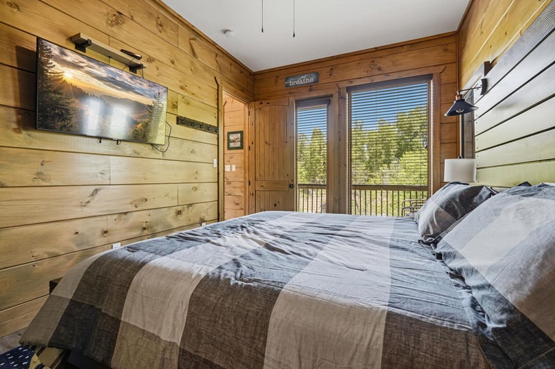 Wake up in your cozy cabin bedroom with warm wood walls and nature views through the French doors.