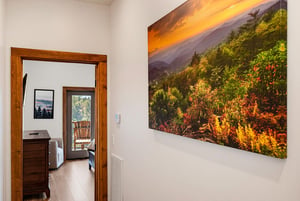 This hallway leads to additional rooms, including a peaceful bedroom retreat. Large wall art featuring a vibrant mountain sunset captures the stunning natural beauty surrounding the property.