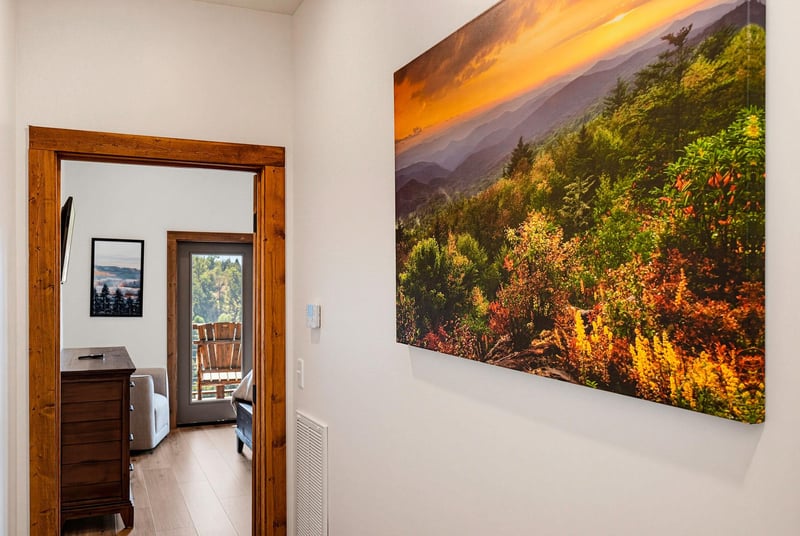 This hallway leads to additional rooms, including a peaceful bedroom retreat. Large wall art featuring a vibrant mountain sunset captures the stunning natural beauty surrounding the property.
