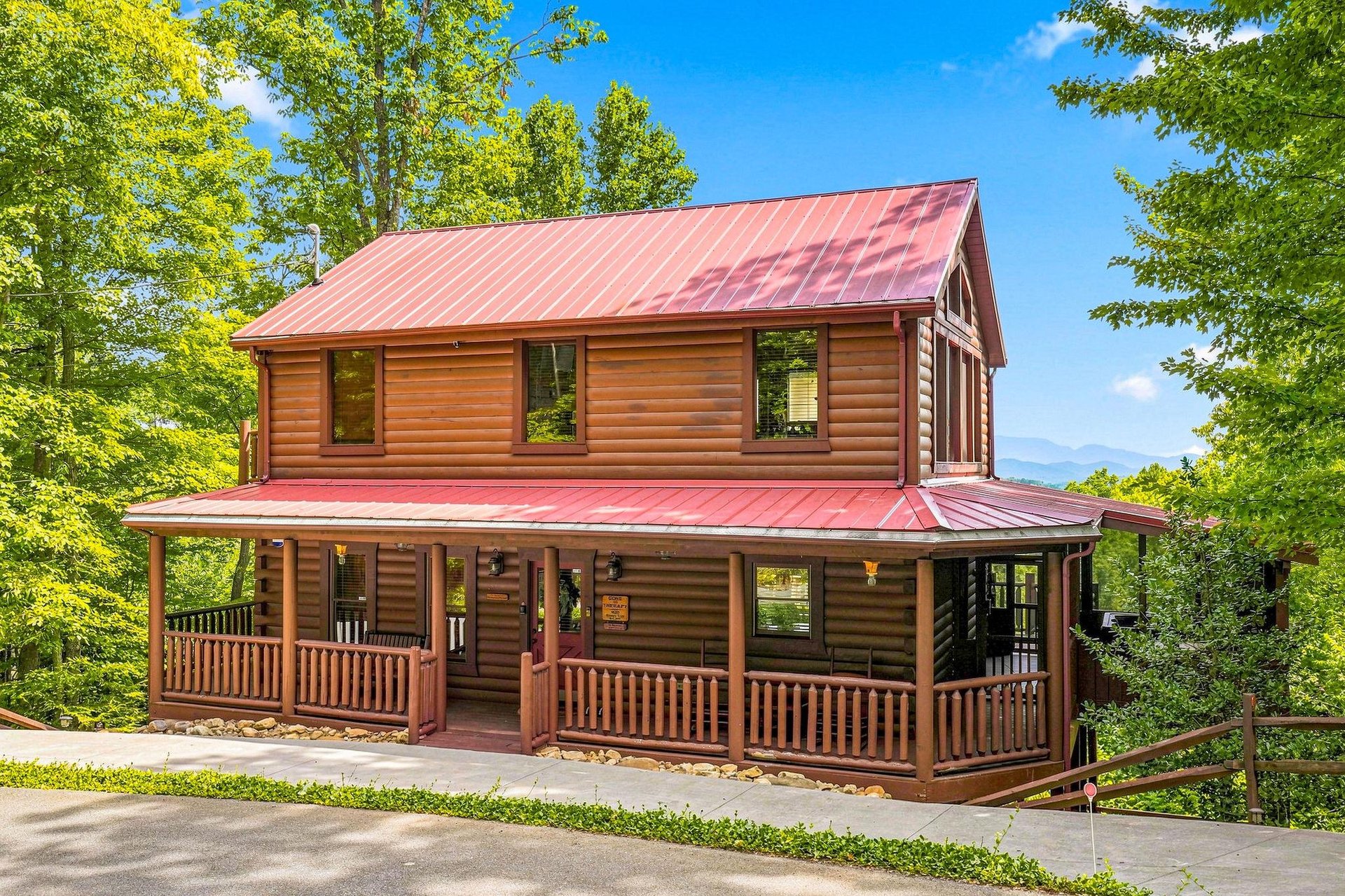 A charming log cabin with a wraparound porch nestled in lush greenery, offering a peaceful mountain escape surrounded by nature.