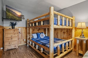 Your rustic bunk bed room features handcrafted log furniture, cozy blue plaid bedding, and a mounted TV for your mountain getaway comfort.