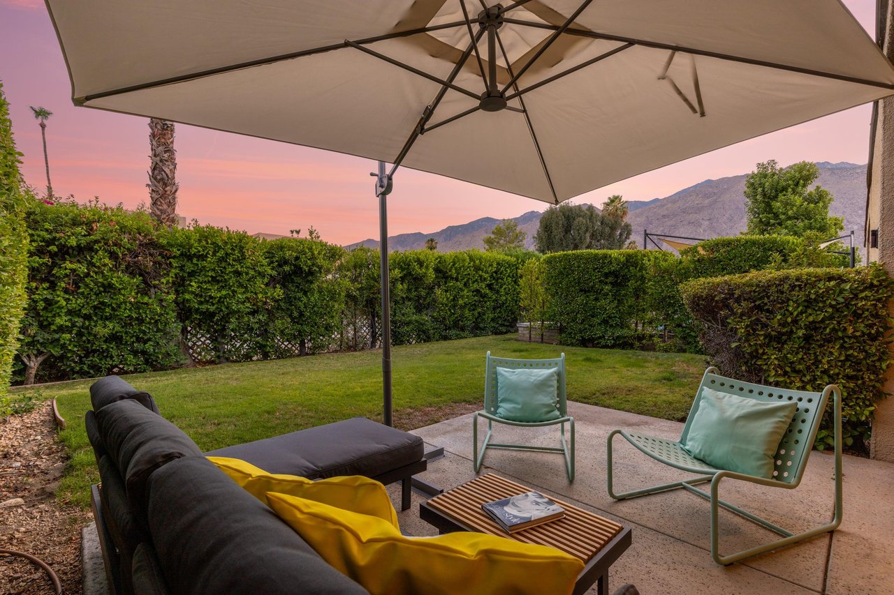 Back patio located off of the living room and primary bedroom featuring a table and chairs for morning coffee, umbrella, and ample outdoor seating.