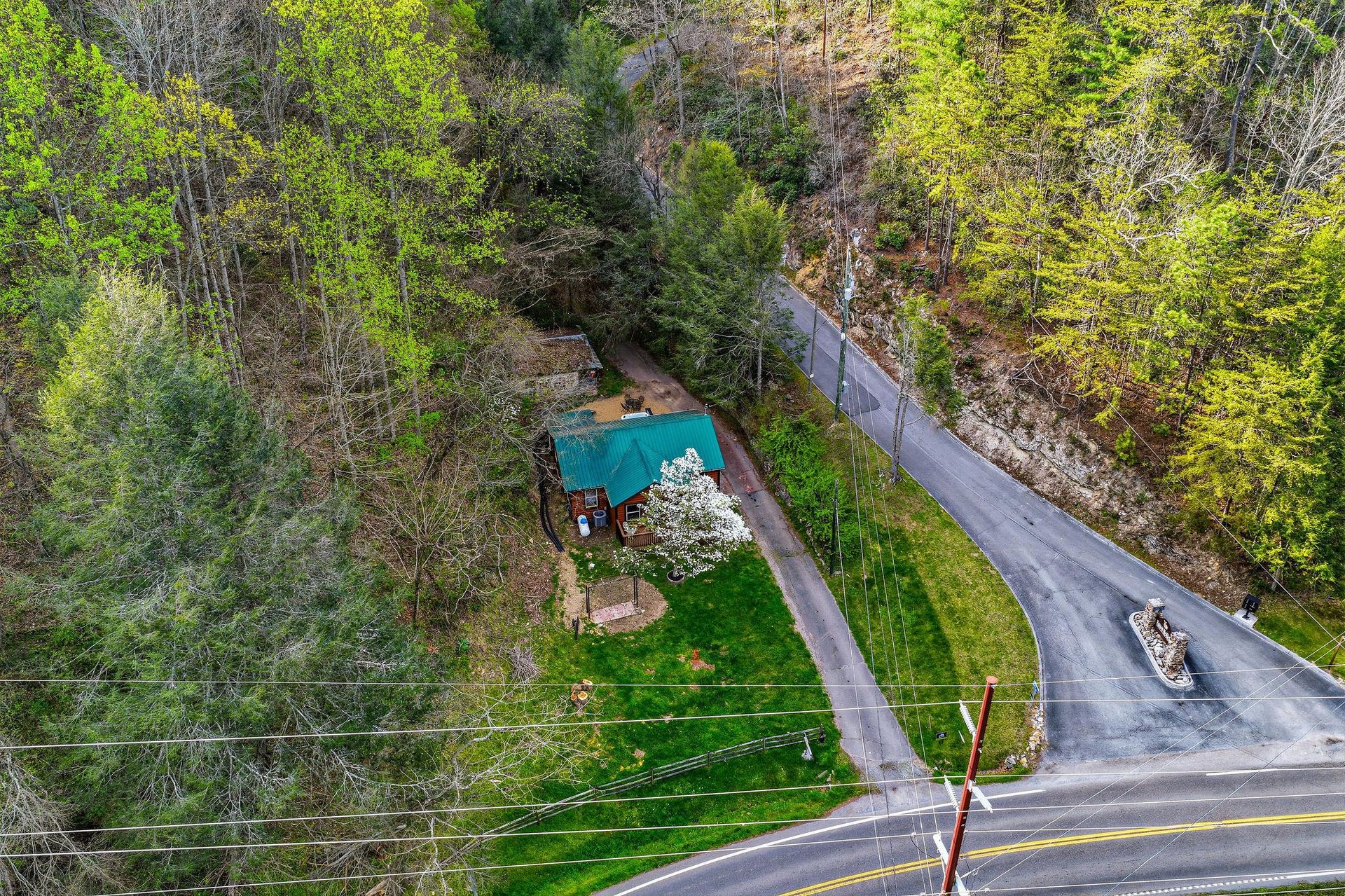 Aerial view of the property nestled among spring trees, featuring a private pool and spacious grounds with direct road access.