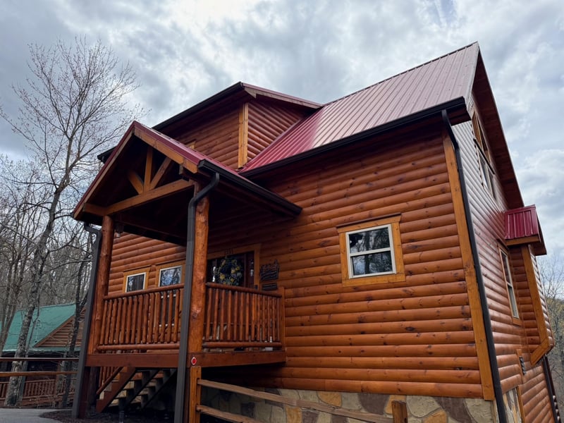 Charming log cabin with warm wood exterior and red metal roof nestled among trees.