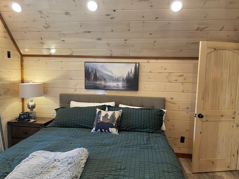 Cozy mountain cabin bedroom with forestgreen bedding and wilderness artwork. Soft lighting creates perfect ambiance for your peaceful retreat.
