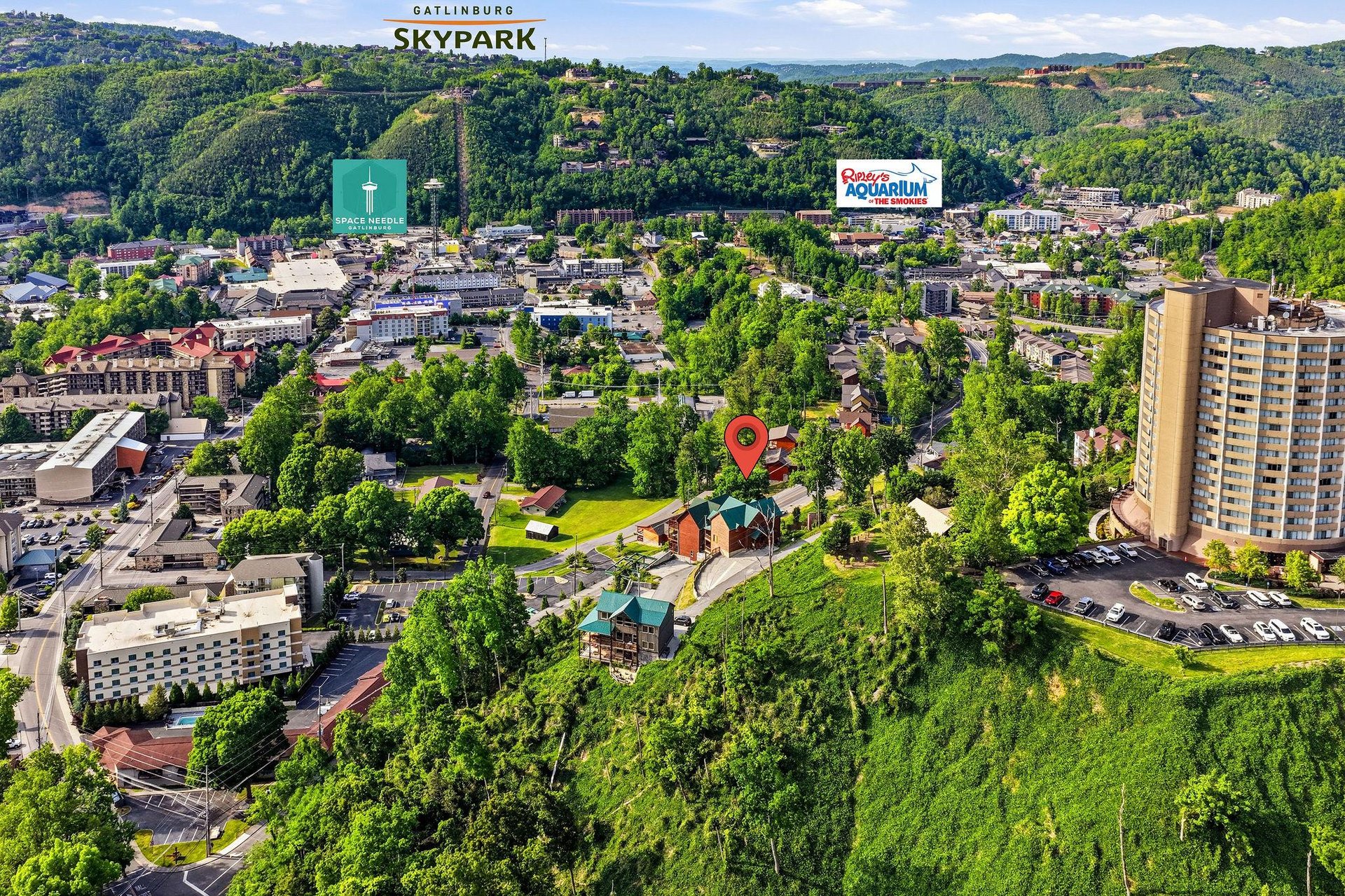 An aerial view of Gatlinburg showcasing the propertys prime location amidst lush green hills and nearby attractions including SkyPark, the Space Needle, and Ripleys Aquarium.