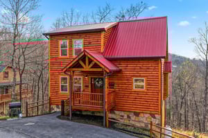 Charming log cabin with red metal roof nestled among bare winter trees, offering a peaceful mountain retreat experience.