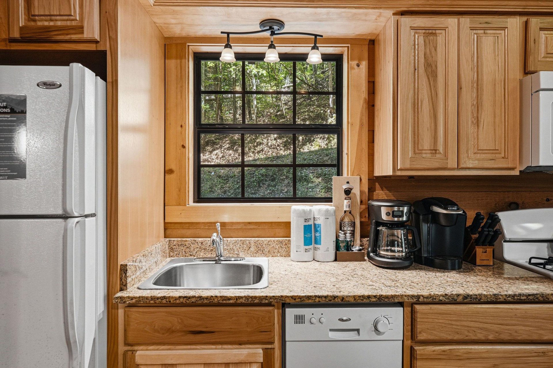 Your fully equipped kitchen features modern appliances, warm wood cabinetry, and a peaceful wooded view—perfect for brewing morning coffee or preparing meals in a cozy, rustic setting.