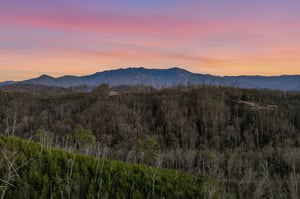 Stunning mountain panorama with vibrant sunset colors painting the sky over forested valleys and distant peaks.