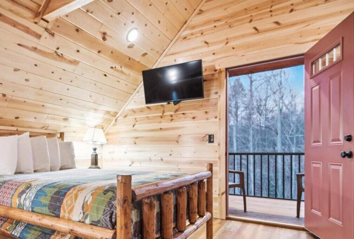 Cozy log cabin bedroom with rustic charm, where youll drift off beneath vaulted ceilings while enjoying wooded views from your private balcony.
