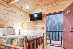 Cozy log cabin bedroom with rustic charm, where youll drift off beneath vaulted ceilings while enjoying wooded views from your private balcony.