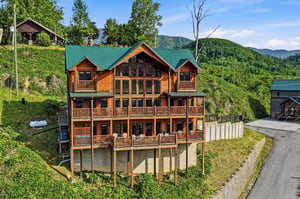 This multistory log cabin rental sits nestled in the lush mountain landscape, offering expansive balconies and large windows to frame the stunning forested peaks surrounding the property.