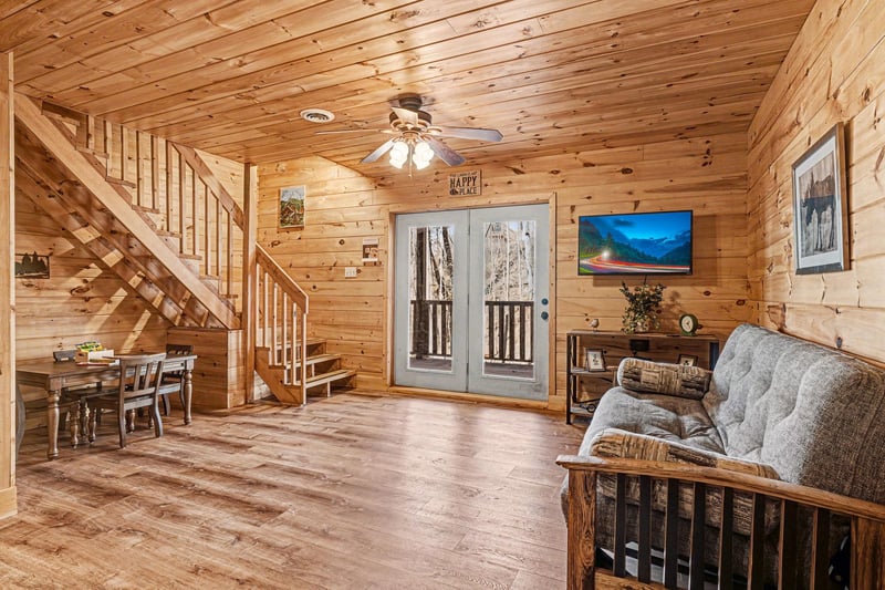 Relax in your cozy cabin living room with rustic wood walls, comfortable seating, and mountain views on the large TV.