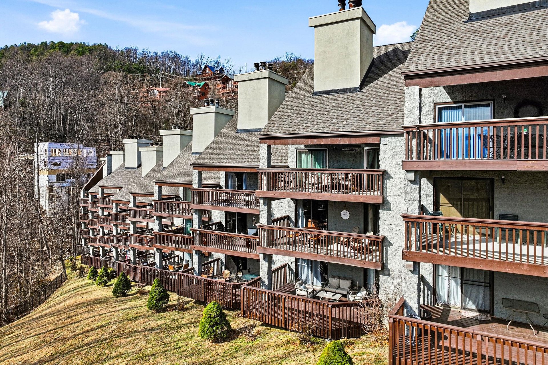 Multilevel property buildings featuring private balconies and terraces nestled among rolling hills and forested mountainside.
