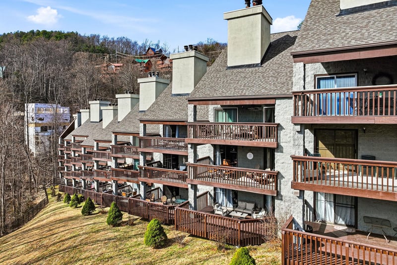 Multilevel property buildings featuring private balconies and terraces nestled among rolling hills and forested mountainside.