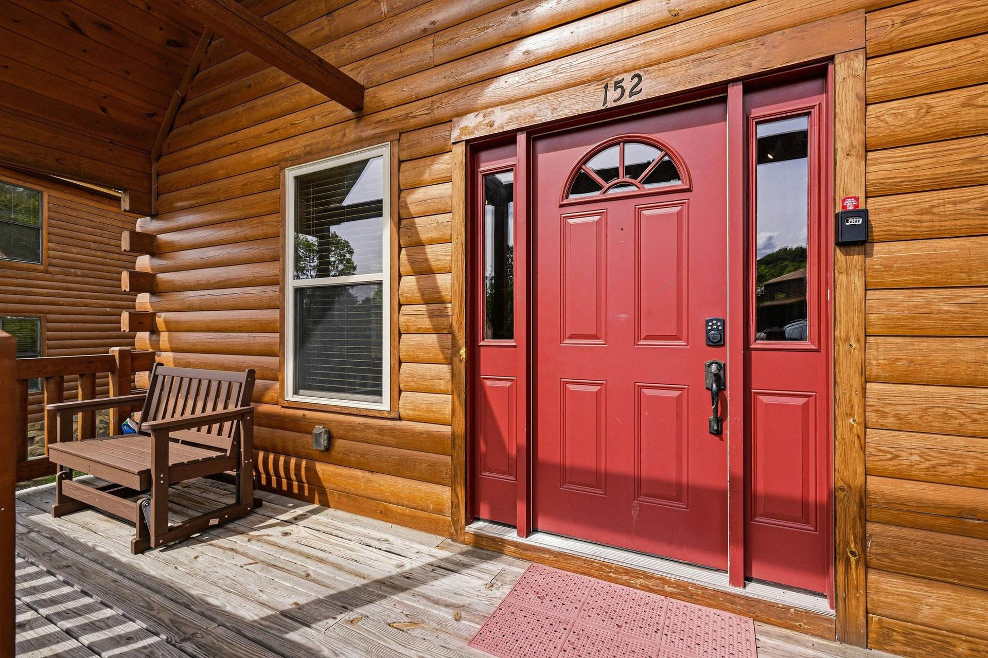 A warm red door marks the entrance to your cozy cabin retreat, with a wooden bench waiting on the porch for quiet moments of relaxation.