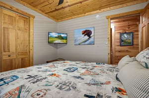 Cozy mountain bedroom with rustic wood finishes, a plush bed with playful winterthemed linens, and warm pine ceilings that invite restful nights.