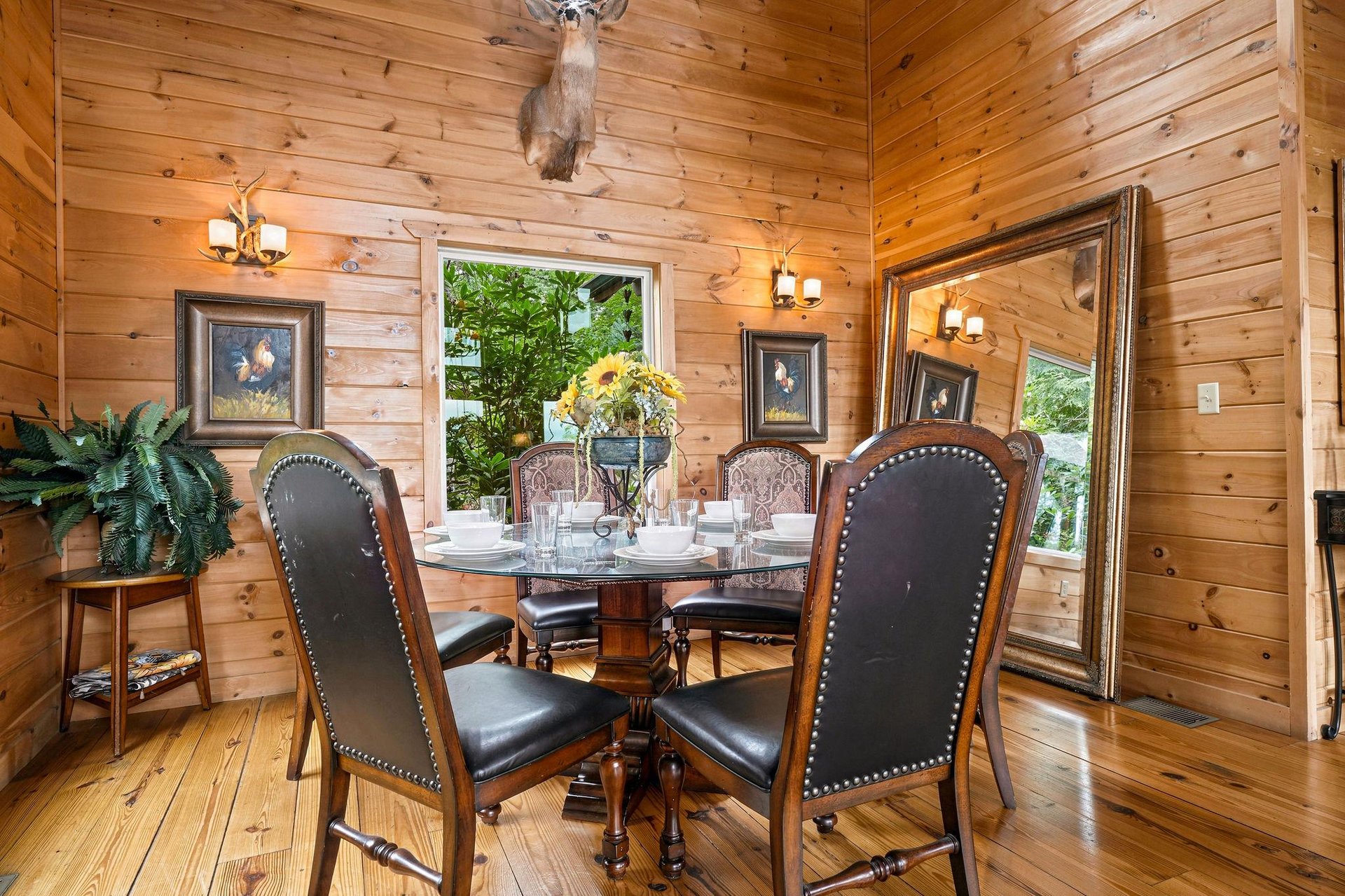 Gather around this elegant dining table beneath rustic wood beams and warm antler lighting. Through large windows, natural greenery frames your meals in a cozy, natureinspired setting.
