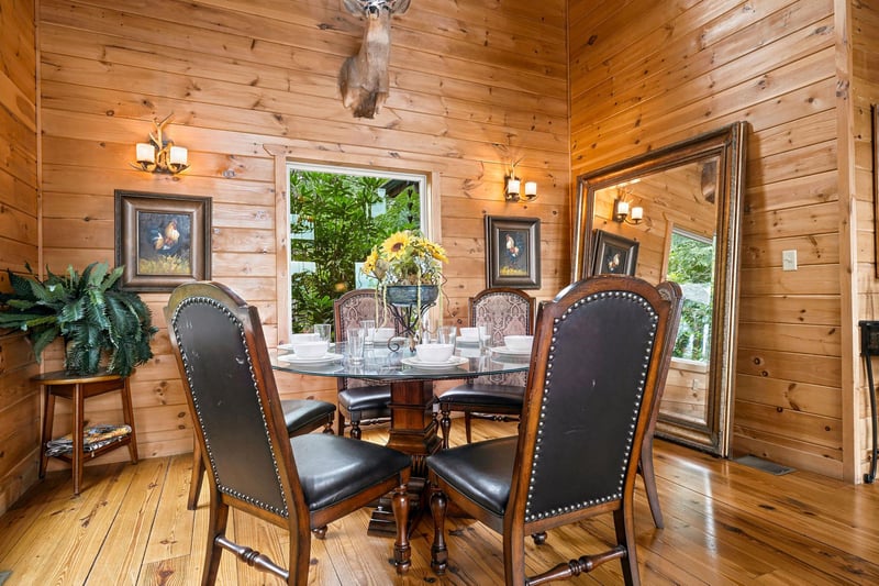 Gather around this elegant dining table beneath rustic wood beams and warm antler lighting. Through large windows, natural greenery frames your meals in a cozy, natureinspired setting.