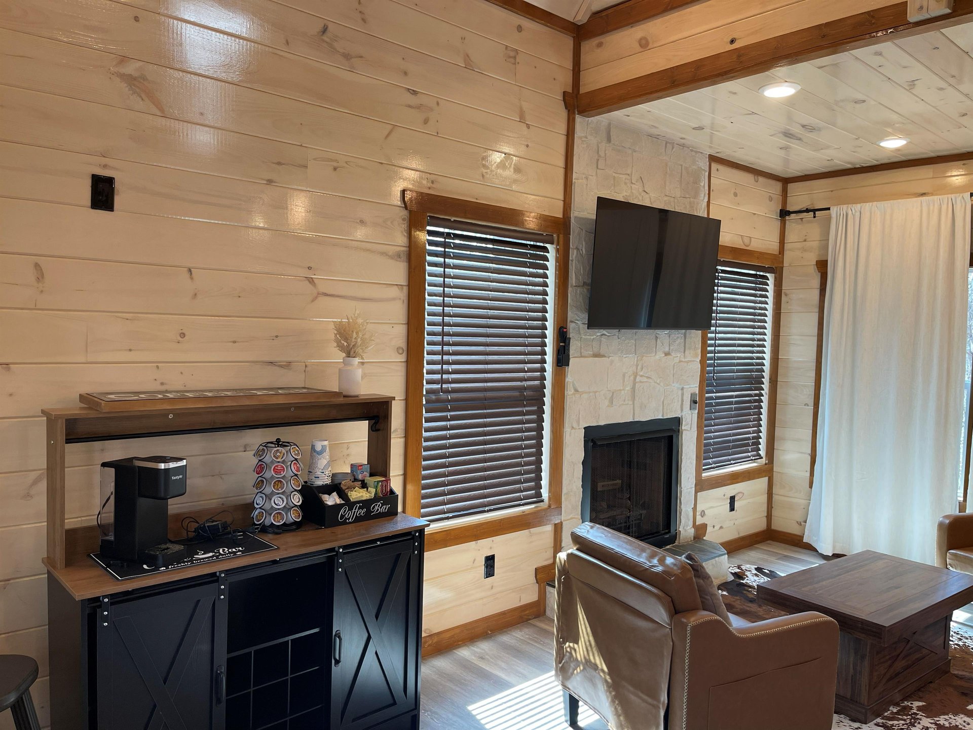 Relax in your cozy living space with rustic wood walls, crackling fireplace, and modern amenities like coffee station and flatscreen TV.