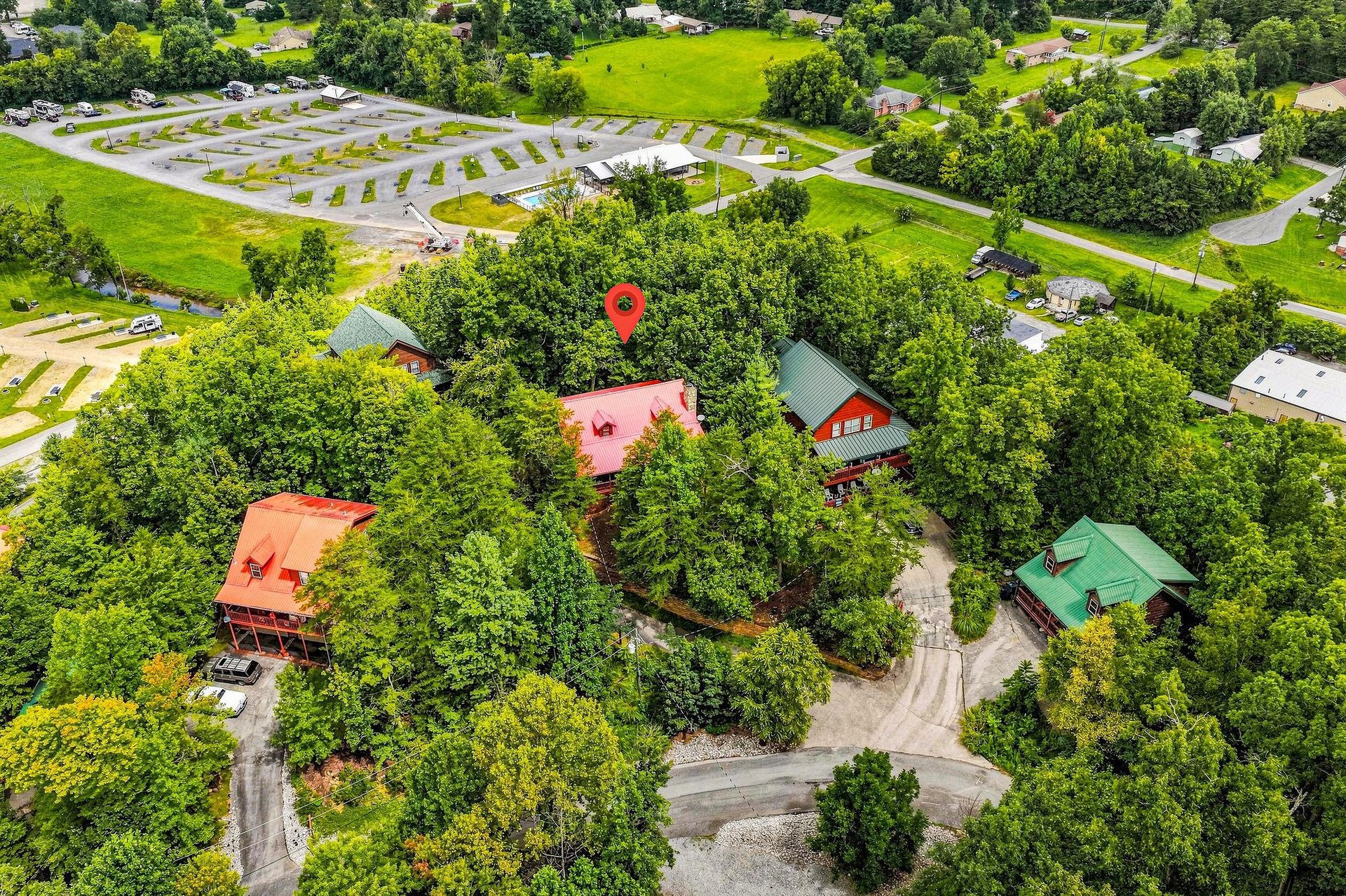 Aerial view of a secluded vacation rental property nestled among lush trees, featuring colorful cabins with metal roofs, private driveways, and nearby parking areas in a quiet residential neighborhood