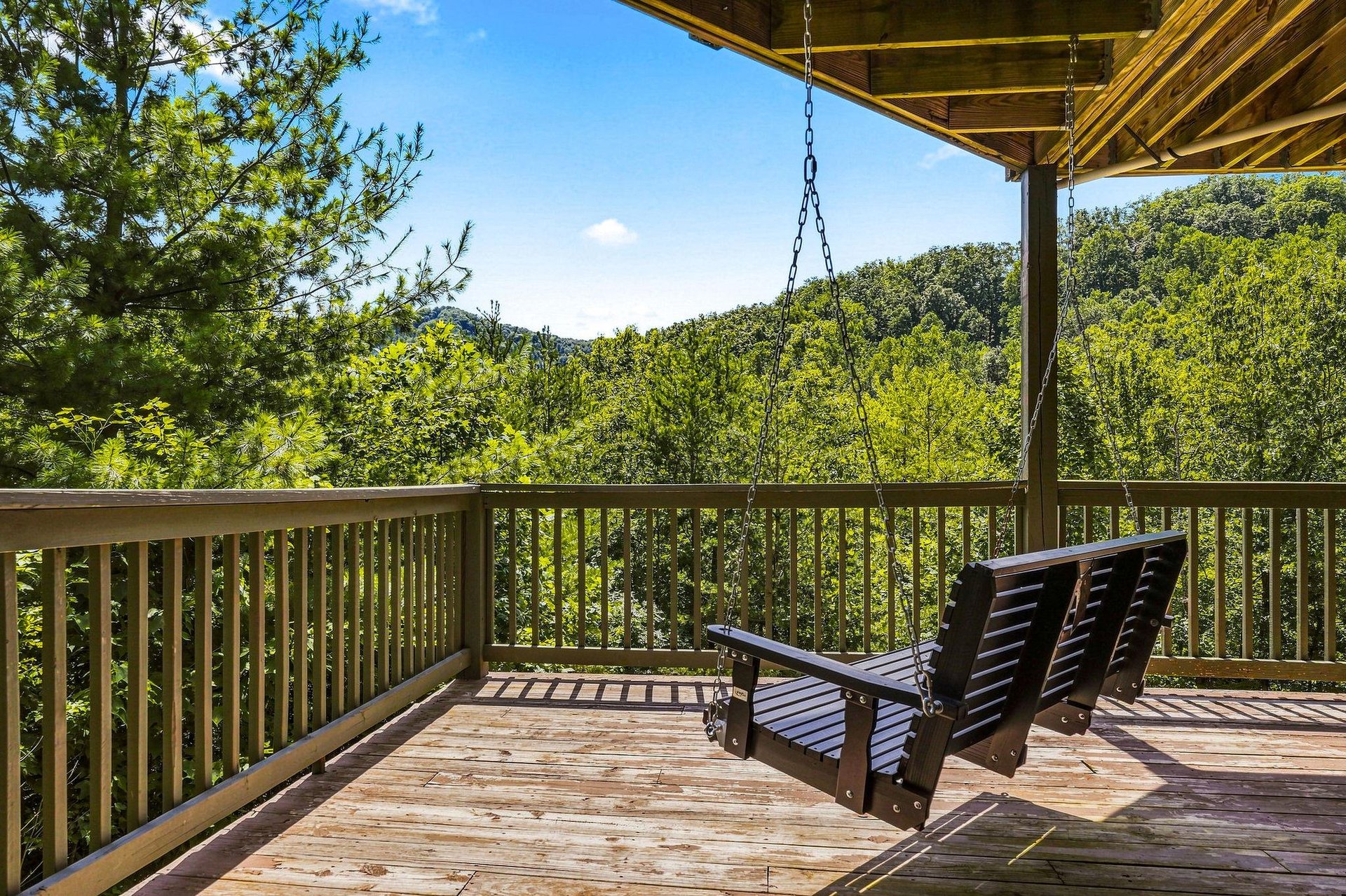Covered deck overlooks rolling wooded hills from the propertys natural surroundings, with a cozy porch swing for taking in the scenic landscape views.