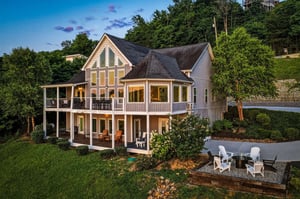 This stunning lakeside retreat features expansive windows, multilevel covered porches, and a private outdoor fire pit area—all nestled among lush greenery and scenic hillside surroundings.