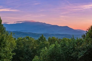 The property sits nestled among rolling mountains and verdant forest, offering sweeping natural landscape views at sunset.