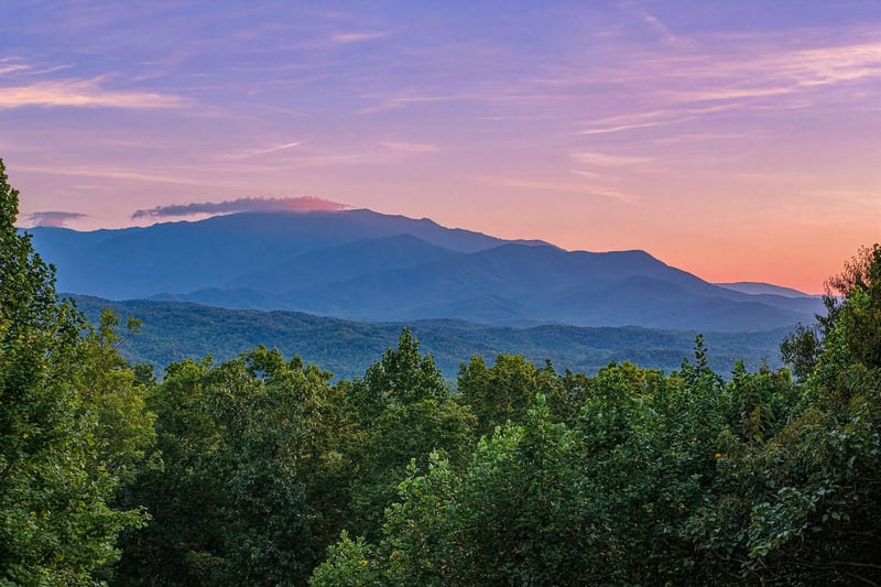The property sits nestled among rolling mountains and verdant forest, offering sweeping natural landscape views at sunset.