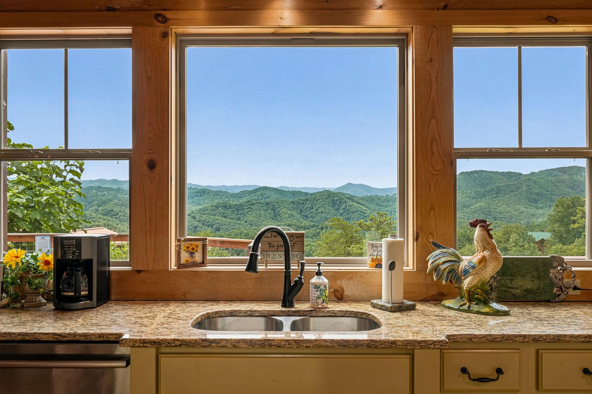 Savor your morning coffee at this kitchen sink with sweeping mountain vistas framed by rustic wood accents and sunlit skies.
