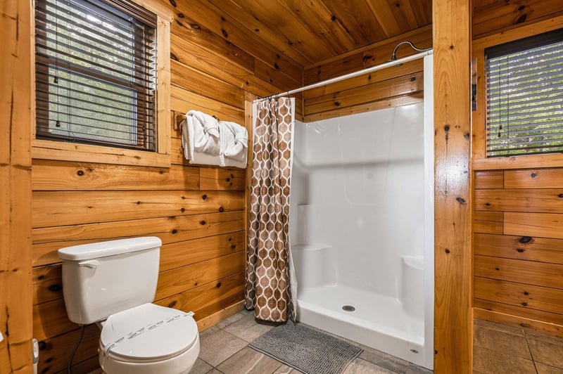 Rinse off in your private bathroom featuring a walkin shower framed by rustic wood walls, complete with plush towels and natural light filtering through the windows.