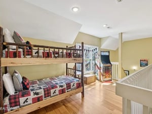 Your kids will love this bright loft bedroom with rustic bunk beds and a classic arcade game for endless entertainment. Cozy plaid quilts and natural wood create a warm mountain retreat feel.