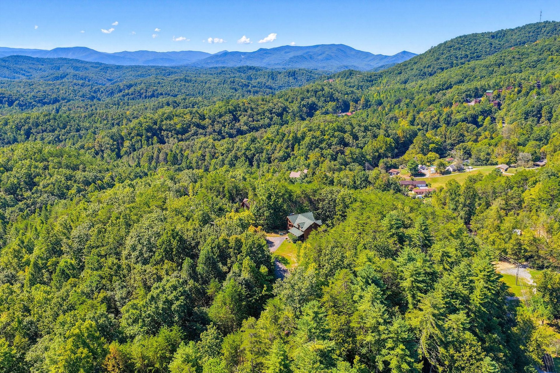 An aerial view reveals the property nestled among lush forests with a breathtaking mountain backdrop stretching across the horizon.