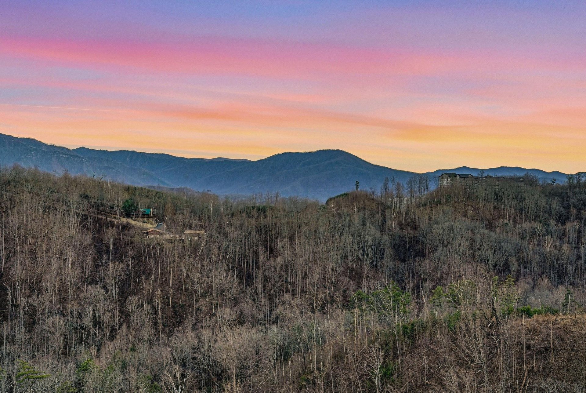 Stunning mountain vista with vibrant sunset colors painting the sky above rolling forested hills and distant peaks.