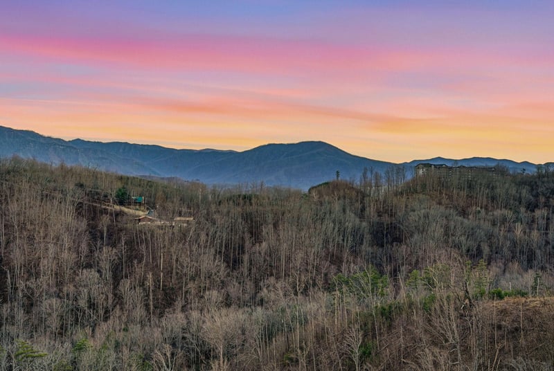 Stunning mountain vista with vibrant sunset colors painting the sky above rolling forested hills and distant peaks.