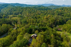 Spectacular aerial view showcases the property nestled among rolling mountain ridges and dense forest canopy in this pristine natural setting.